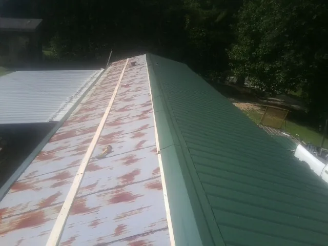 Old rusted panels beside newly installed green metal roofing — Wind Damage Roof Repair by Roofing Brothers in Twin Bridges