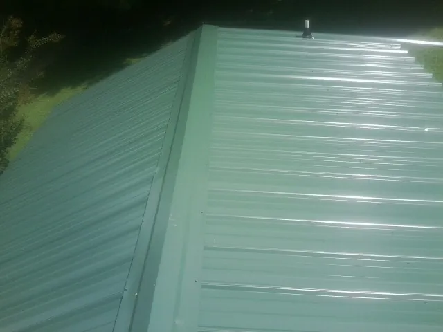 New green metal panels meeting at the ridge of a roof — Flat Roof Repair work by our crew in Twin Bridges