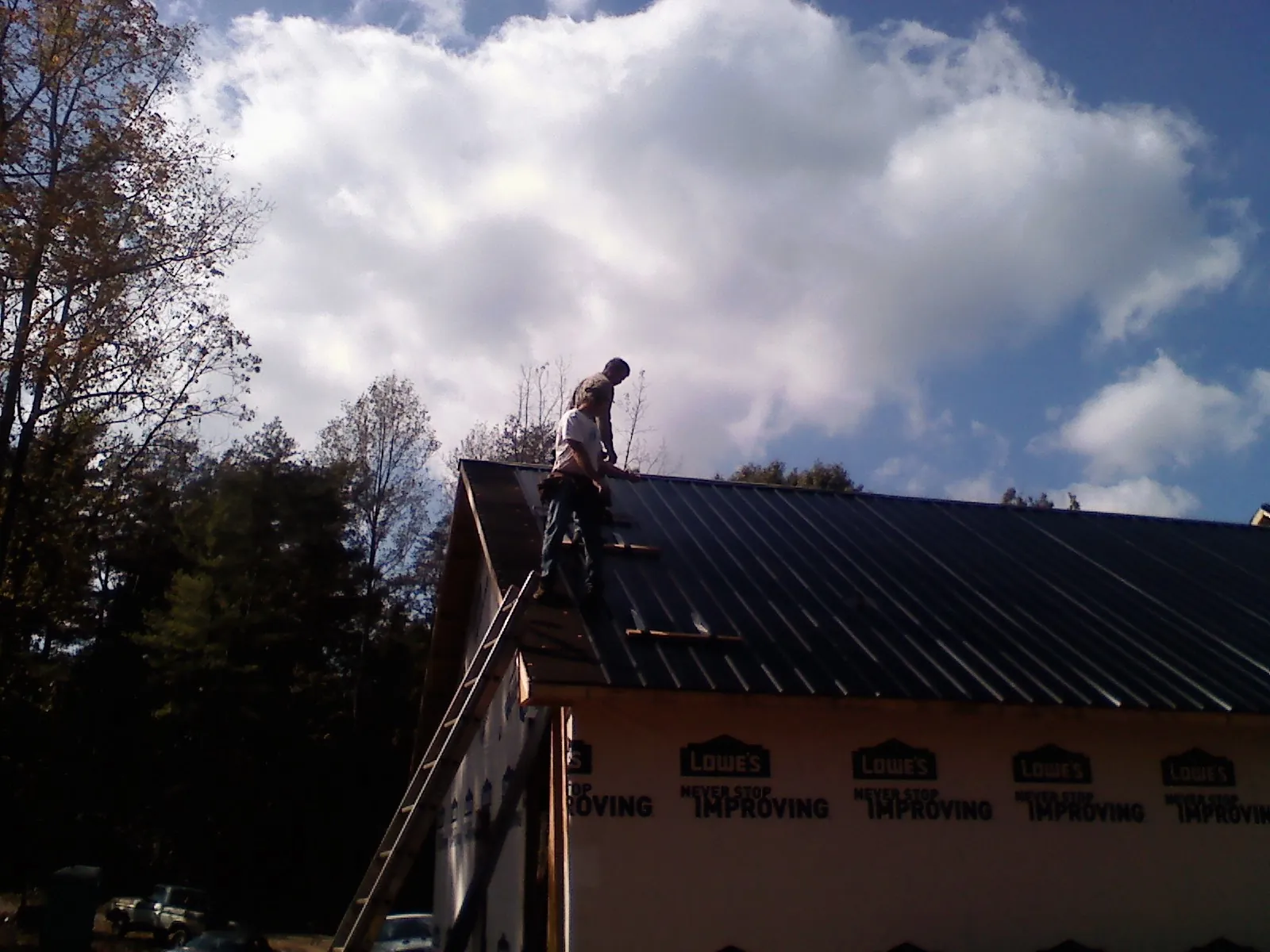 Roofer fastening dark metal panels high against a cloudy sky, from a Roof Inspection job in Twin Bridges