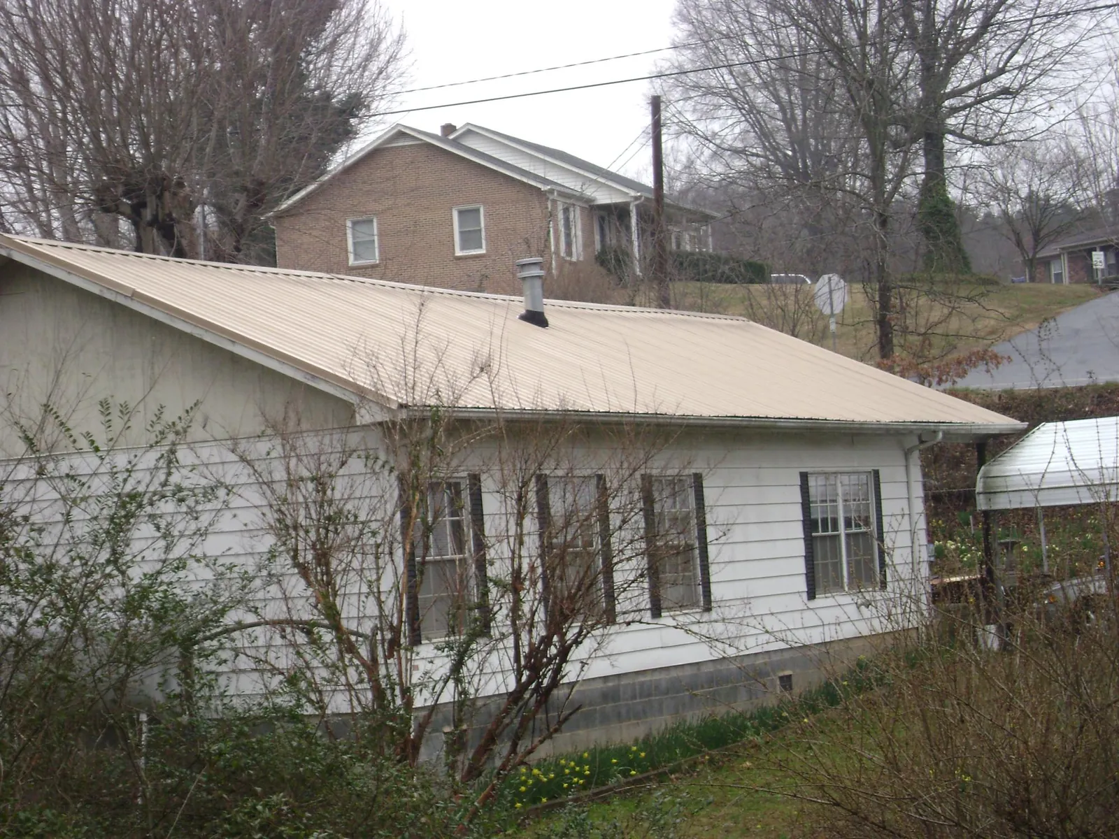 Tan metal roof on a white sided house set into a hillside — Commercial Roofing by Roofing Brothers in Twin Bridges