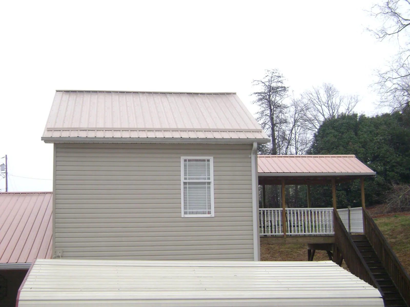Tan metal roofs on a two story addition and attached porch, from a Roof Replacement job in Twin Bridges
